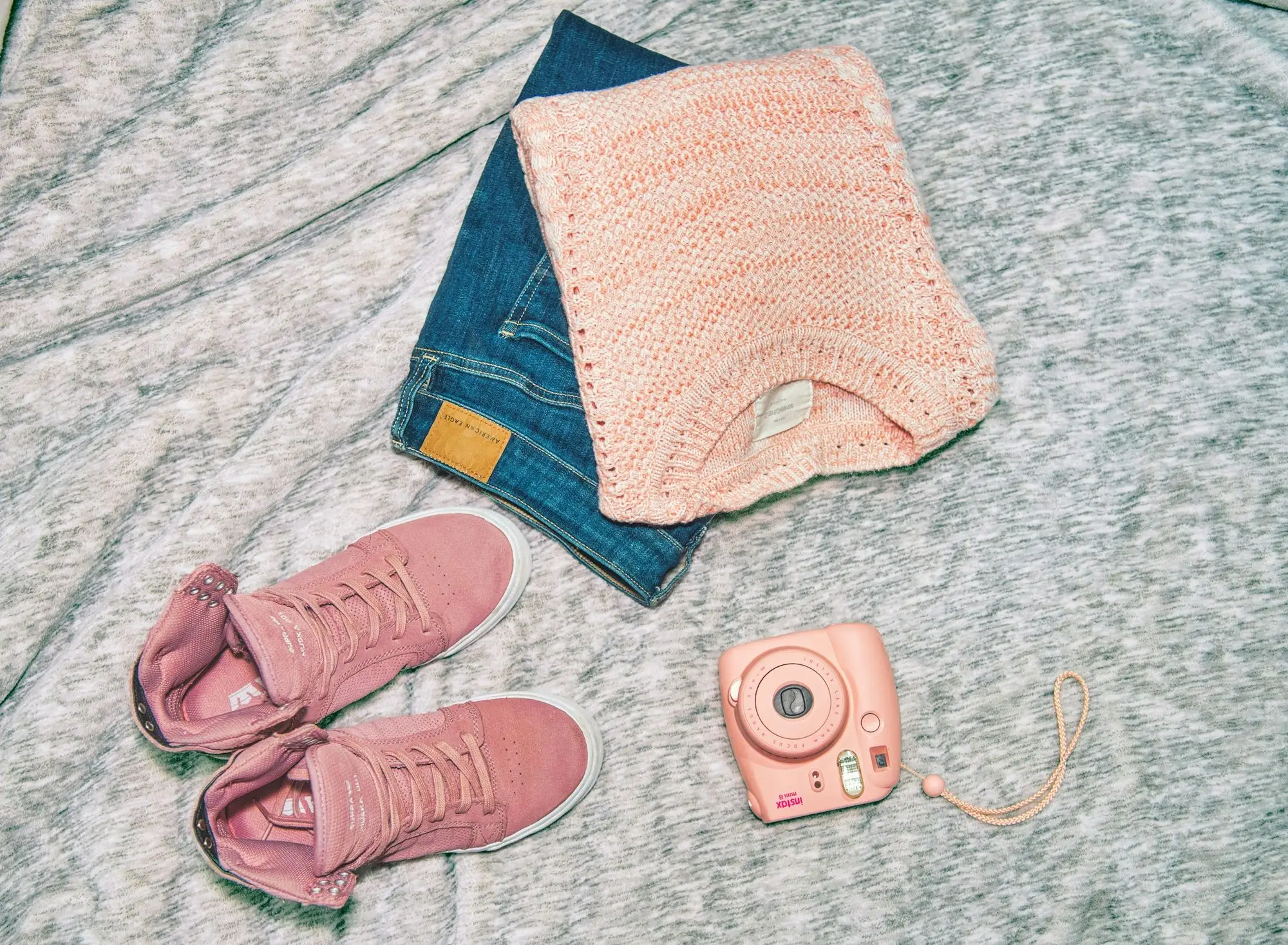 A flat lay of jeans, a pink knit, pink trainers and an instant camera
