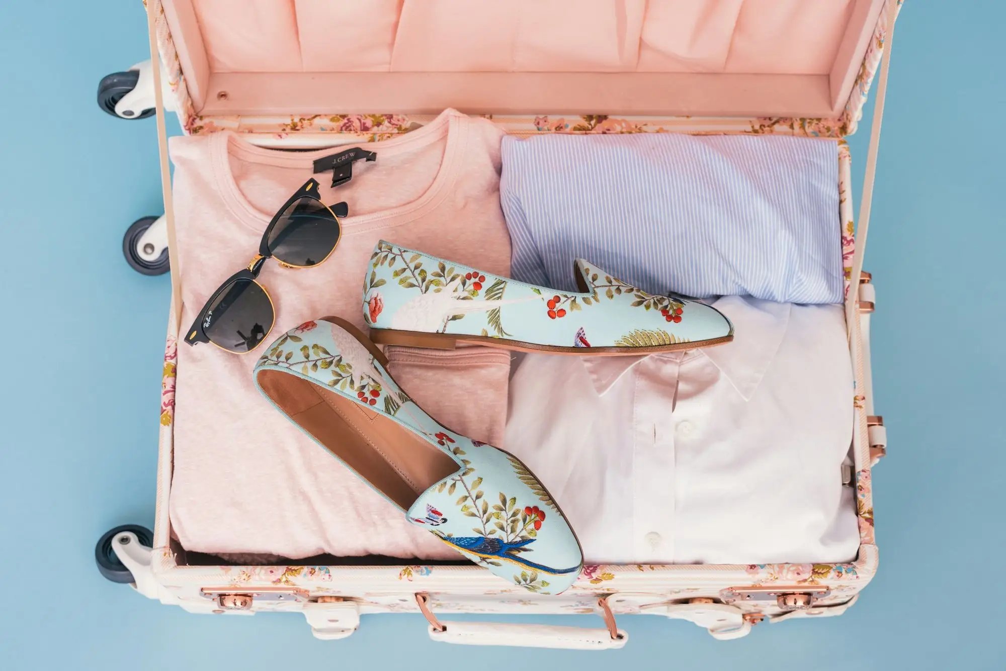 A pink suitcase packed with pastel clothes, sunglasses and shoes